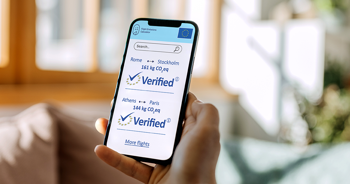 Person holding a phone. The screen displays the verified checkmark of the flight emissions label next to the carbon emissions of flights.